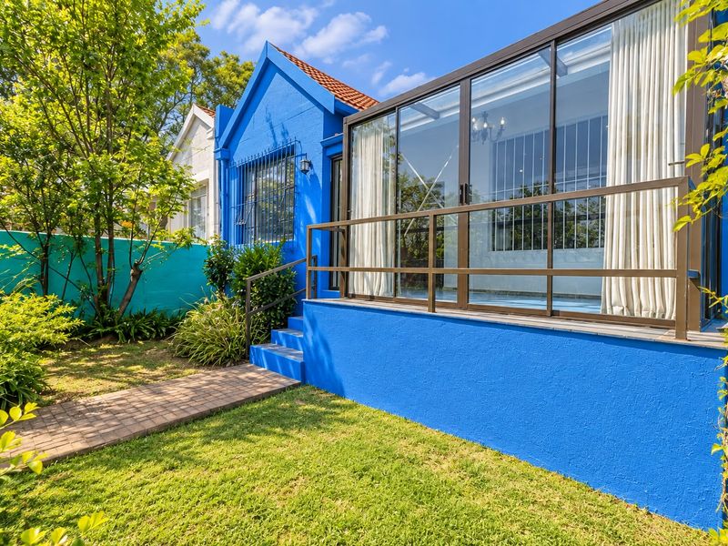 Rear view of the property featuring a vibrant blue exterior, a paved garden path, and an enclosed glass patio area with metal railings.