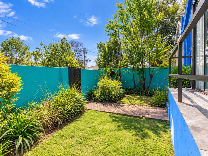 A well-maintained private garden featuring a lush lawn, paved pathway, and vibrant boundary wall, providing a pleasant outdoor space.