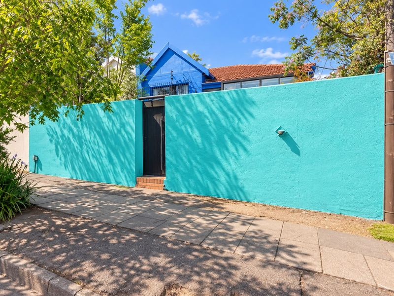 Front view of the property featuring a vibrant turquoise boundary wall, a secure pedestrian gate, and a glimpse of the blue house structure behind.