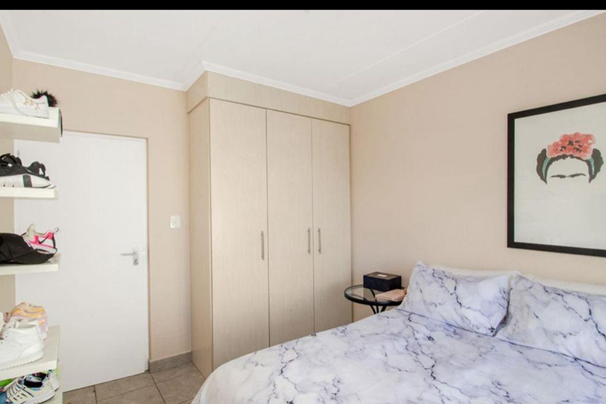 A well-maintained bedroom featuring neutral walls, tiled flooring, and a functional built-in wardrobe for storage.