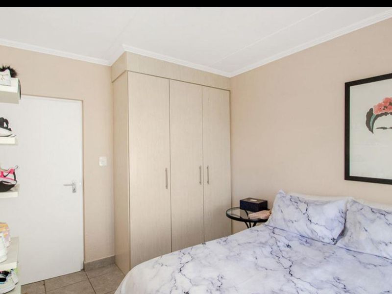 A well-maintained bedroom featuring neutral walls, tiled flooring, and a functional built-in wardrobe for storage.