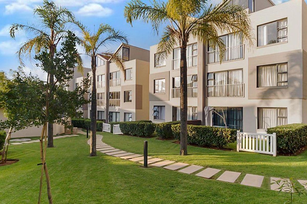 A well-maintained apartment complex exterior featuring landscaped gardens, paved walkways, and private balconies with sliding glass doors.
