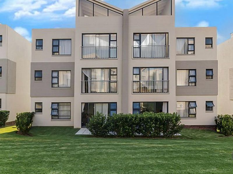 Rear elevation of a modern apartment complex featuring multiple levels with balconies, large sliding glass doors, and well-maintained surrounding lawn.