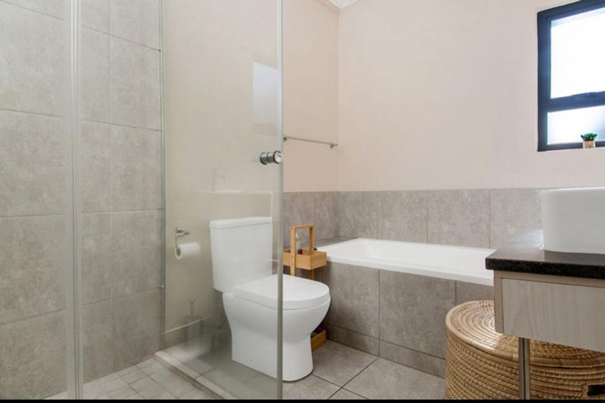Modern bathroom featuring a glass-enclosed shower, built-in bathtub, vanity basin, and neutral floor-to-ceiling tiling.