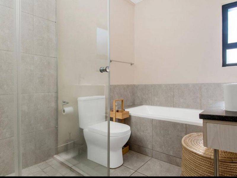 Modern bathroom featuring a glass-enclosed shower, built-in bathtub, vanity basin, and neutral floor-to-ceiling tiling.