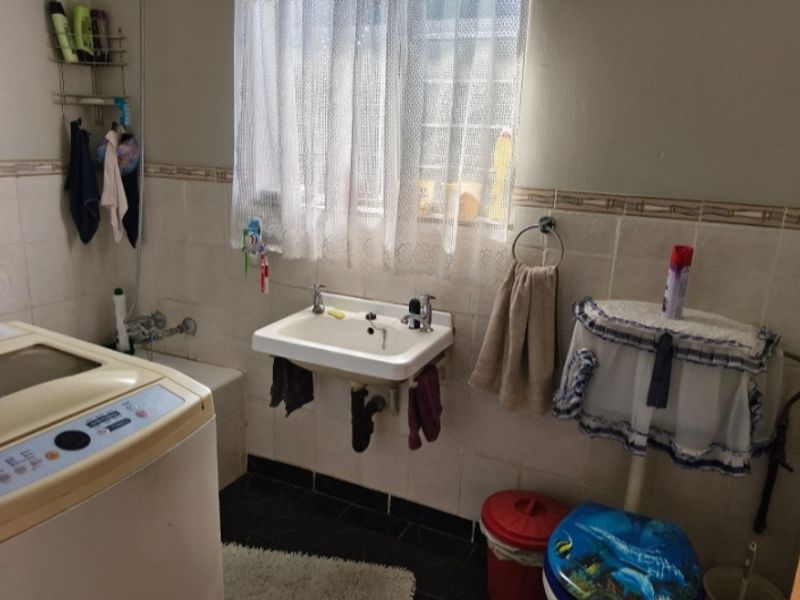 A functional bathroom featuring a wall-mounted basin, toilet, and tiled finishes, requiring cosmetic updates to modernize the space.