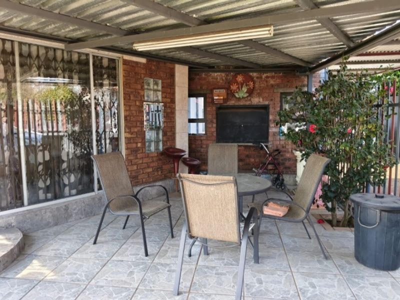 Covered outdoor patio area featuring a built-in braai, tiled flooring, and direct access to the home through a large glass sliding door.