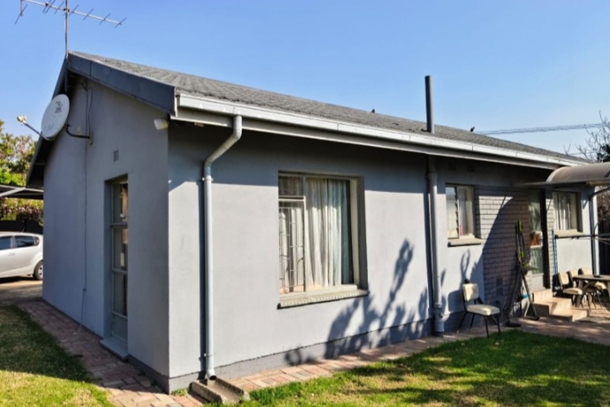 Rear view of a single-story house featuring a pitched roof, painted brick exterior, and paved walkway leading along the side of the building.