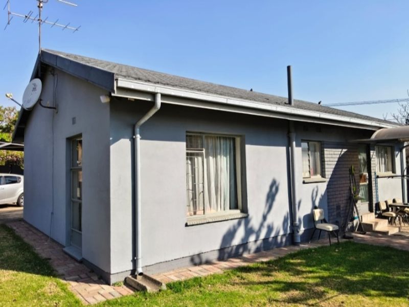 Rear view of a single-story house featuring a pitched roof, painted brick exterior, and paved walkway leading along the side of the building.