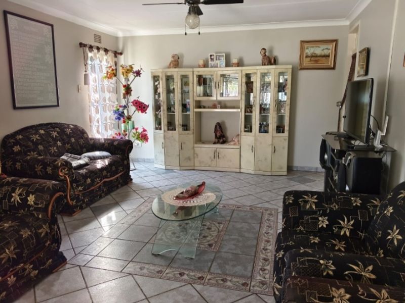 A spacious living room featuring tiled flooring, a ceiling fan, and decorative cove cornicing, providing a functional and comfortable family living area.