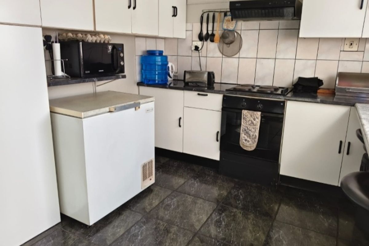 A functional kitchen featuring white cabinetry, dark countertops, tiled backsplash, and built-in electric cooking appliances with dark floor tiles.