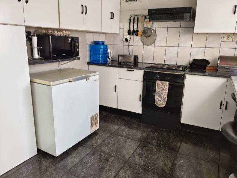 A functional kitchen featuring white cabinetry, dark countertops, tiled backsplash, and built-in electric cooking appliances with dark floor tiles.