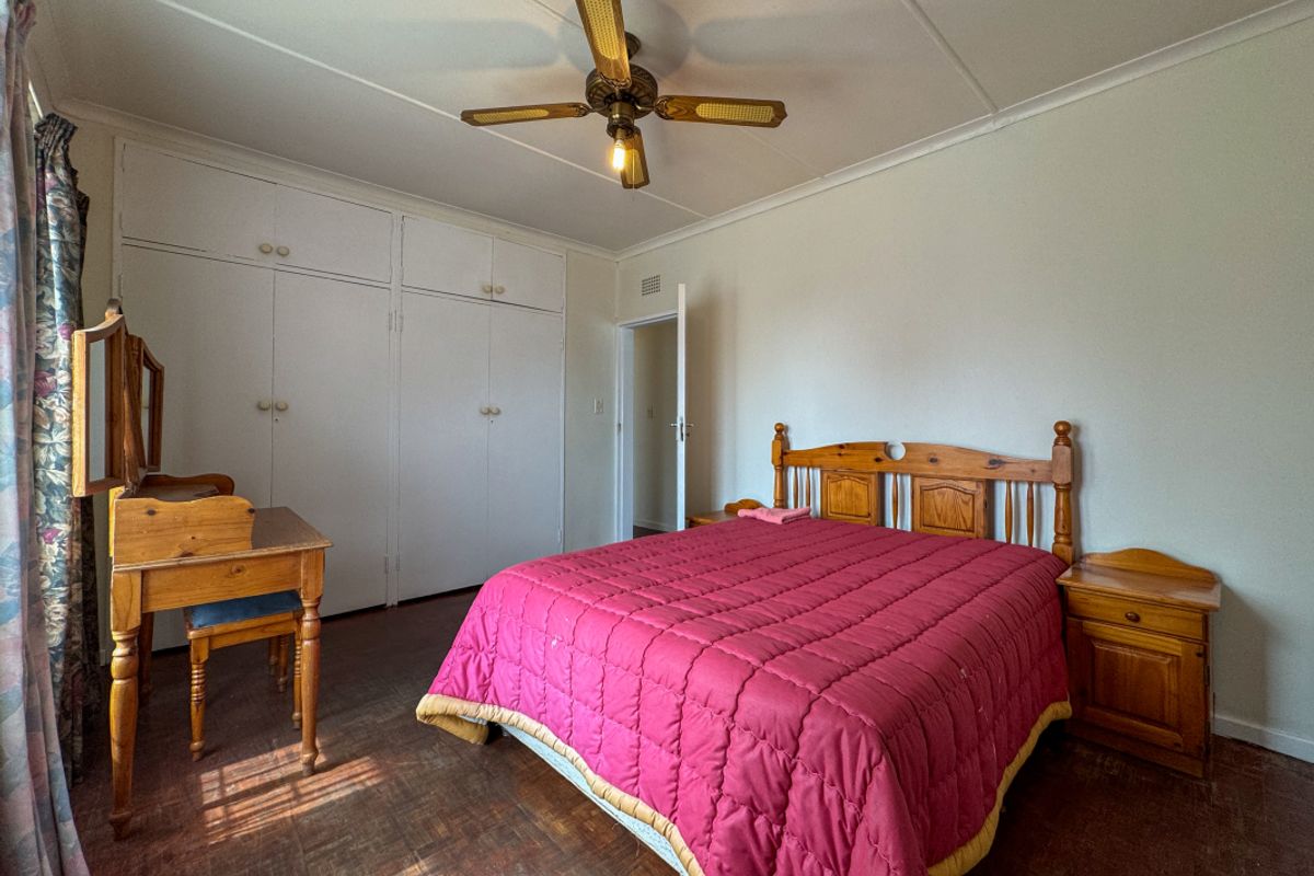 A spacious bedroom featuring built-in cupboards, a ceiling fan, and traditional parquet flooring, offering a functional layout with potential for modern updates.