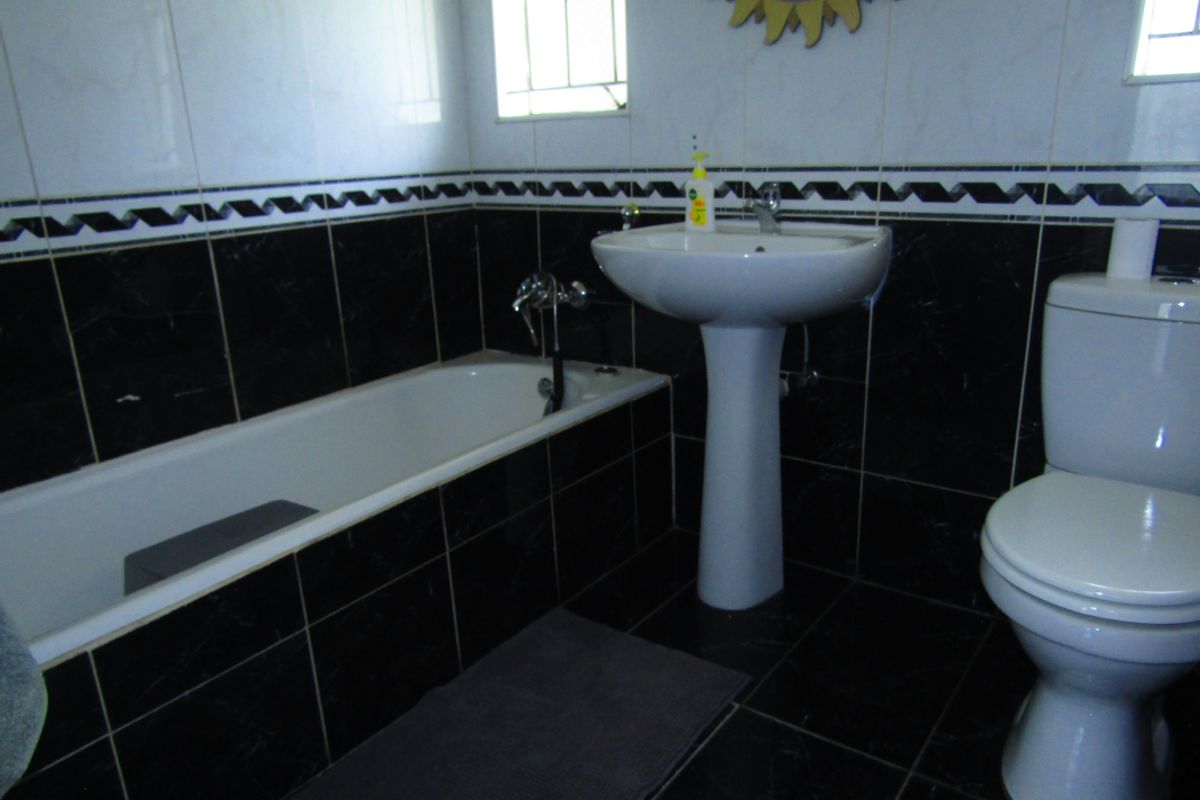 A functional bathroom featuring a pedestal basin, bathtub, and toilet with contrasting black and white wall and floor tiling.