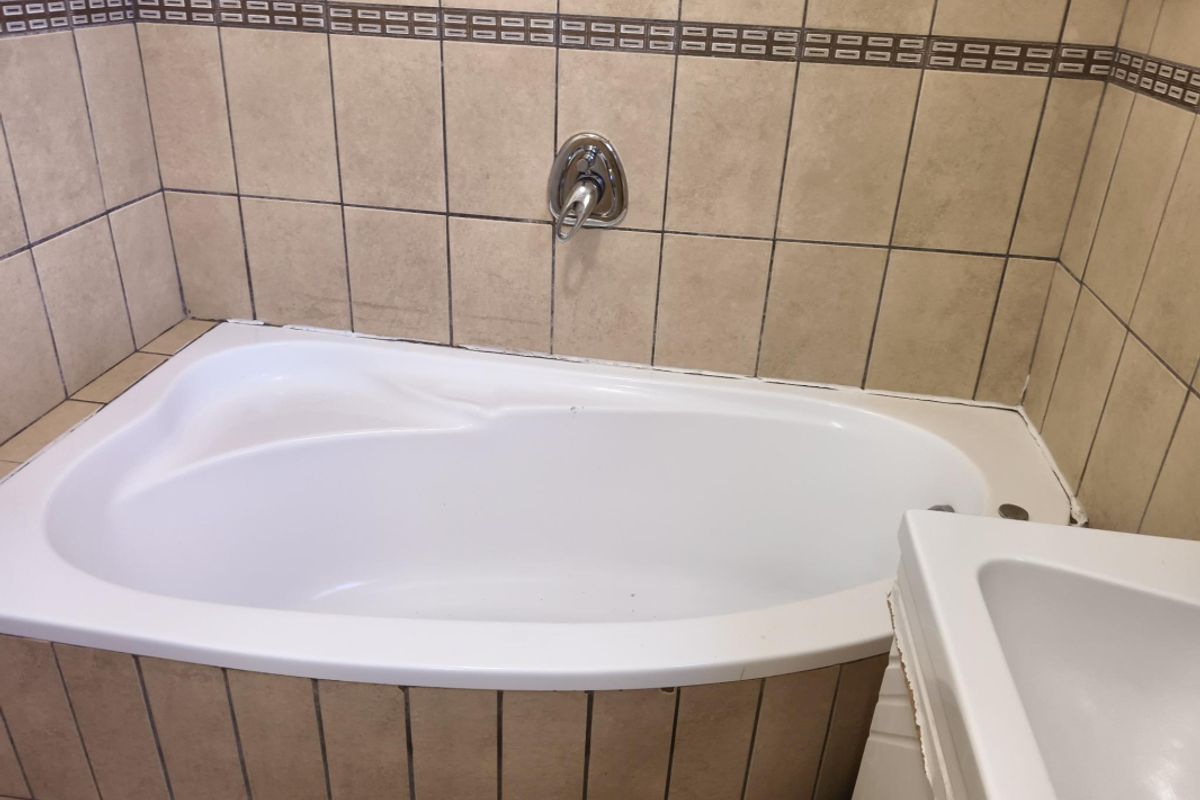 A bathroom featuring a built-in bathtub with wall-mounted mixer tap and neutral ceramic wall tiling.