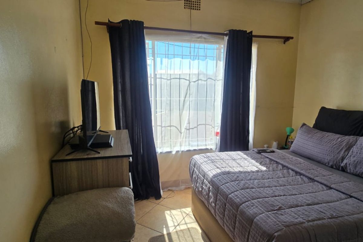 A bedroom featuring tiled flooring and a window fitted with security bars, requiring cosmetic updates to the wall finishes.
