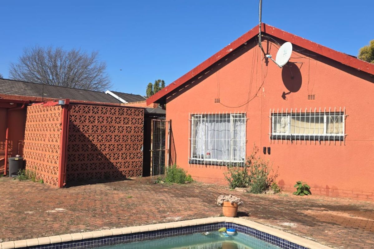 Rear exterior view of the property featuring a swimming pool, brick paved area, and security bars on windows.