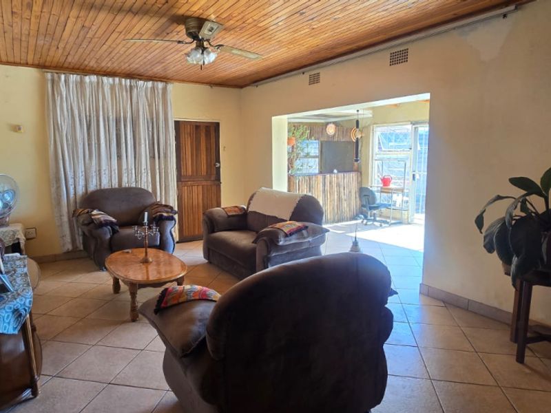 Living room featuring a timber ceiling, tiled floors, and a brick fireplace, with an open transition to an adjacent sunroom area.