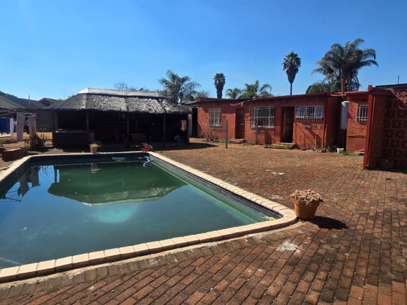 Outdoor pool area featuring a swimming pool, paved patio, and a thatched lapa structure in the rear garden.