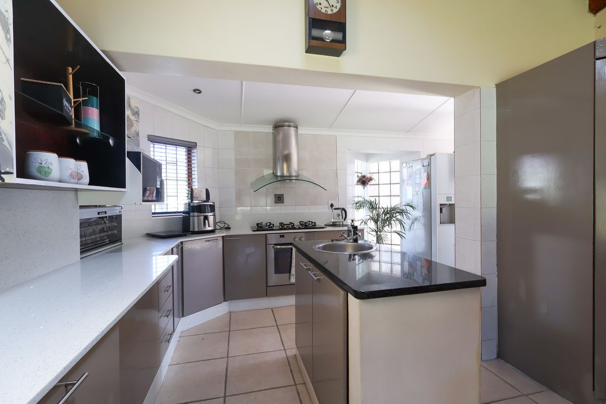 A functional kitchen featuring a central island, stone countertops, gas hob with extractor, and tiled flooring, offering a practical layout for cooking and preparation.