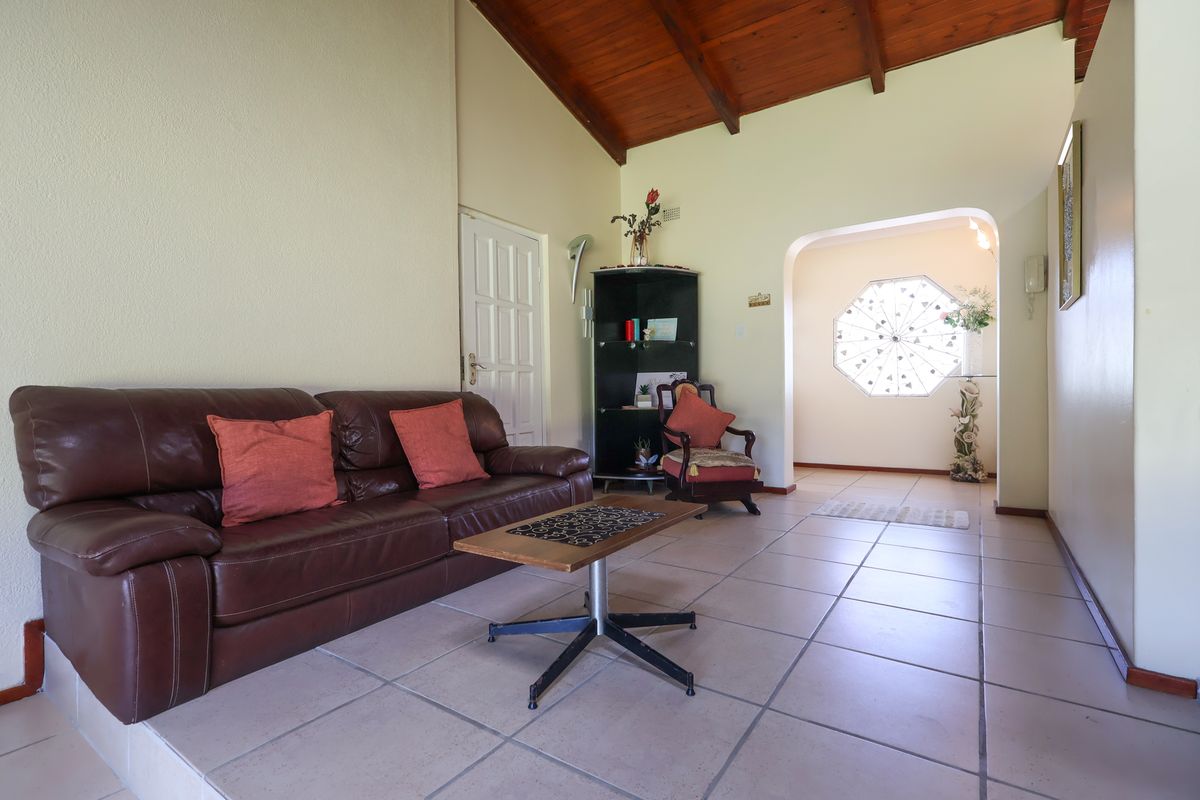 Spacious living area featuring high exposed timber rafter ceilings, ceramic floor tiles, and a unique decorative octagonal window in the adjacent hallway.