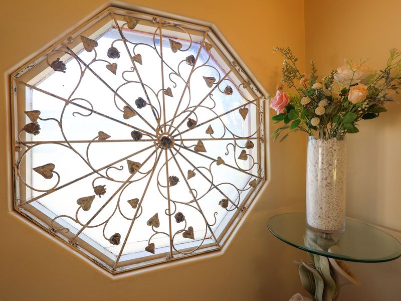 A close-up view of an octagonal window featuring a decorative metal grille, set within a neutral-toned interior wall.