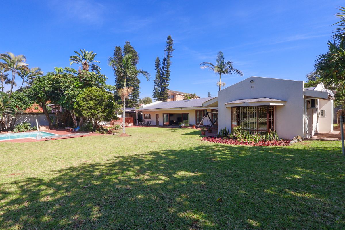 Spacious rear garden featuring a well-maintained lawn, swimming pool, and direct access to the home via large sliding doors.