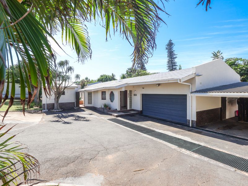 Front exterior view of the house featuring a garage, attached carport, and a paved driveway with mature palm trees.