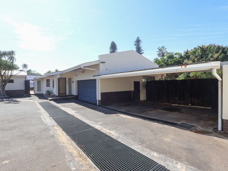 Front exterior view of the property featuring a paved driveway, integrated garage, and a covered carport area with a timber privacy screen.