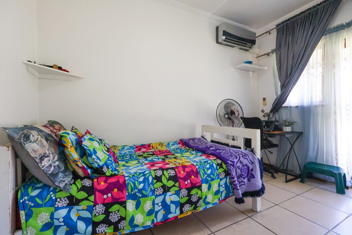 A functional bedroom featuring tiled flooring, a wall-mounted air conditioning unit, and security gate on the window.