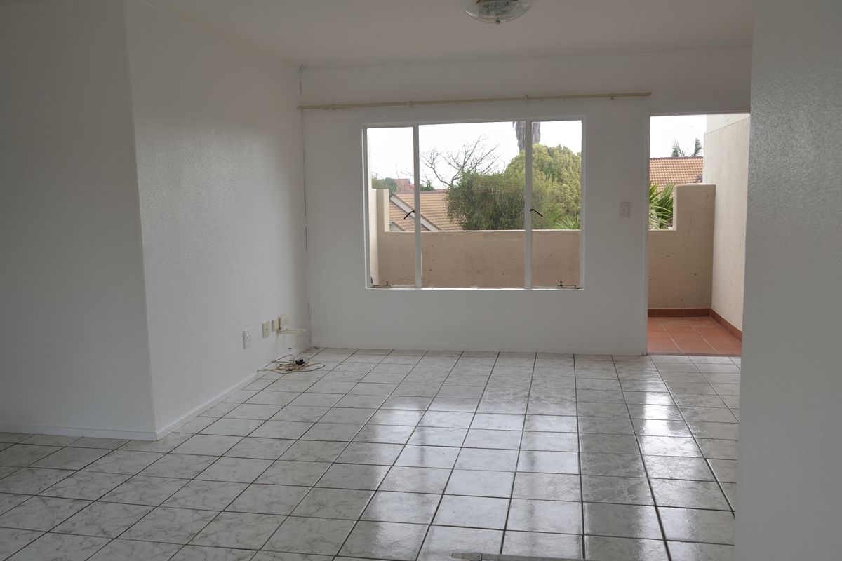 An empty, open-plan living area featuring tiled flooring, neutral walls, and direct access to an outdoor balcony space.