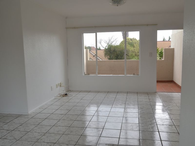 An empty, open-plan living area featuring tiled flooring, neutral walls, and direct access to an outdoor balcony space.