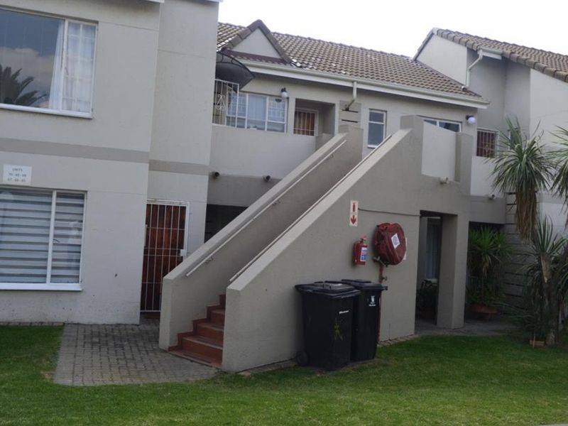 Exterior view of an apartment complex featuring a concrete staircase, tiled roof, and communal garden area with paved access paths.