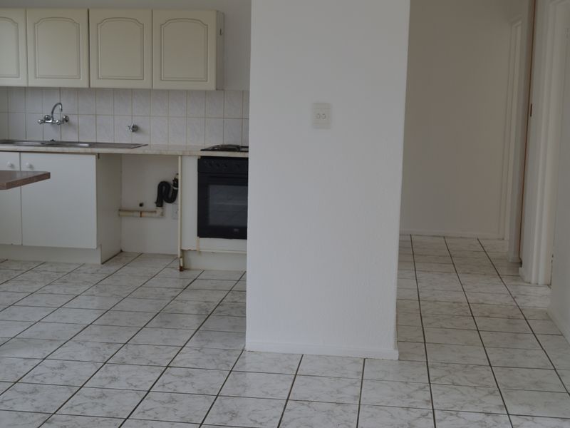A dated, empty kitchen featuring tiled flooring, built-in cabinetry, and an integrated oven, requiring cosmetic updates and repairs to the plumbing area.