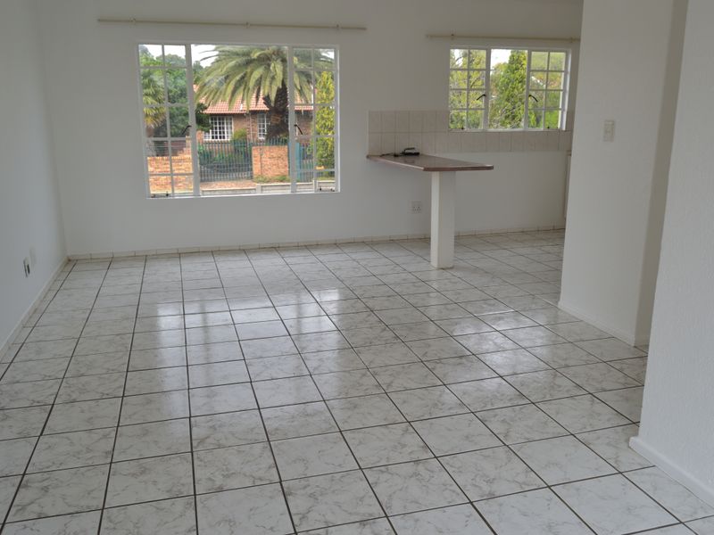 An open-plan living and kitchen area featuring neutral tiled flooring, a built-in breakfast bar, and large windows providing natural light.