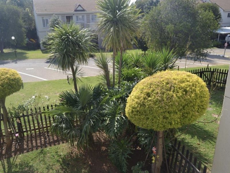 An elevated view overlooking a well-maintained garden area with mature trees and shrubs, enclosed by a picket fence.
