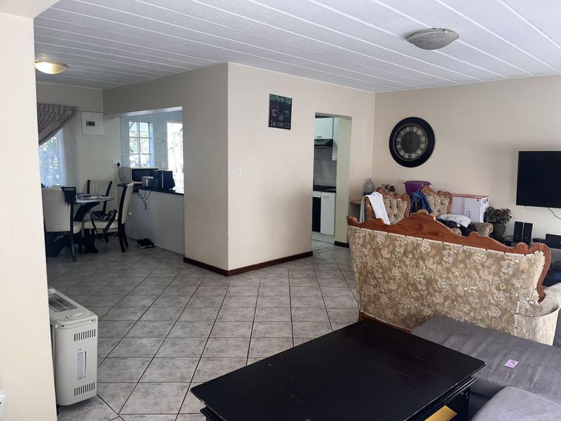 Open-plan living and dining area featuring tiled flooring, a pass-through kitchen window, and neutral wall finishes.