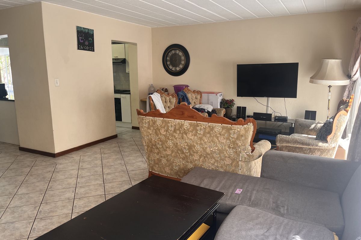 A spacious living room featuring tiled flooring and a textured ceiling, with an open-plan layout leading to the kitchen area.