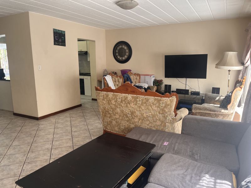 A spacious living room featuring tiled flooring and a textured ceiling, with an open-plan layout leading to the kitchen area.