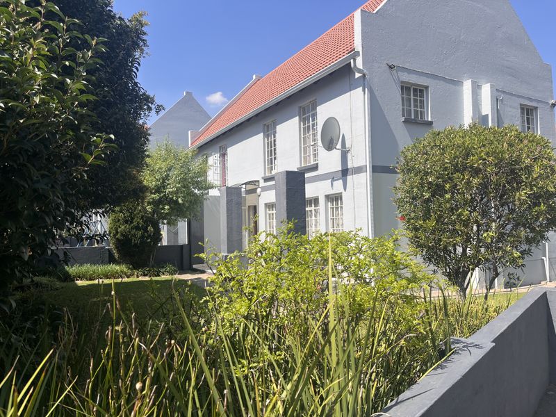 A view of the rear elevation of the townhouse, featuring a terracotta tiled roof, multi-pane windows, and a well-maintained garden area.