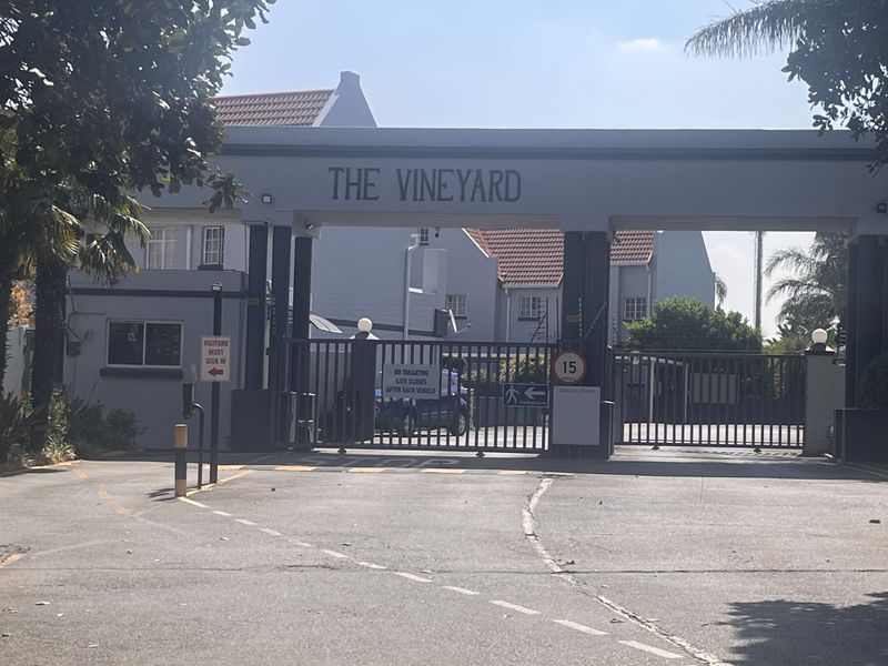 The secure gated entrance to The Vineyard townhouse complex, featuring a controlled access gate and paved driveway approach.