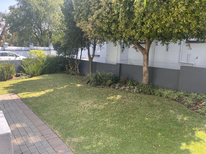 A well-maintained private garden area featuring a neat lawn, established trees, a paved walkway, and secure boundary walling with electric fencing.