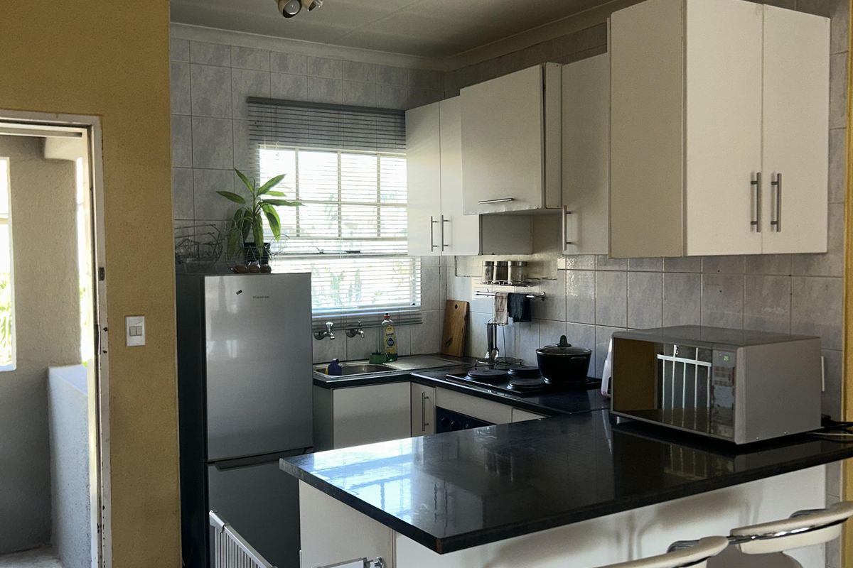 Compact kitchen featuring white cabinetry, dark granite countertops, tiled backsplash, and ceramic flooring with direct access to an outdoor balcony area.