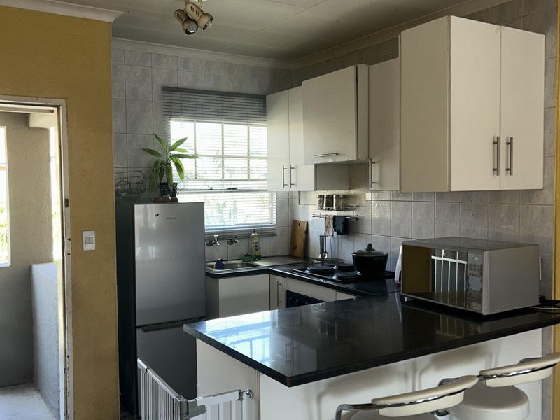 Compact kitchen featuring white cabinetry, dark granite countertops, tiled backsplash, and ceramic flooring with direct access to an outdoor balcony area.