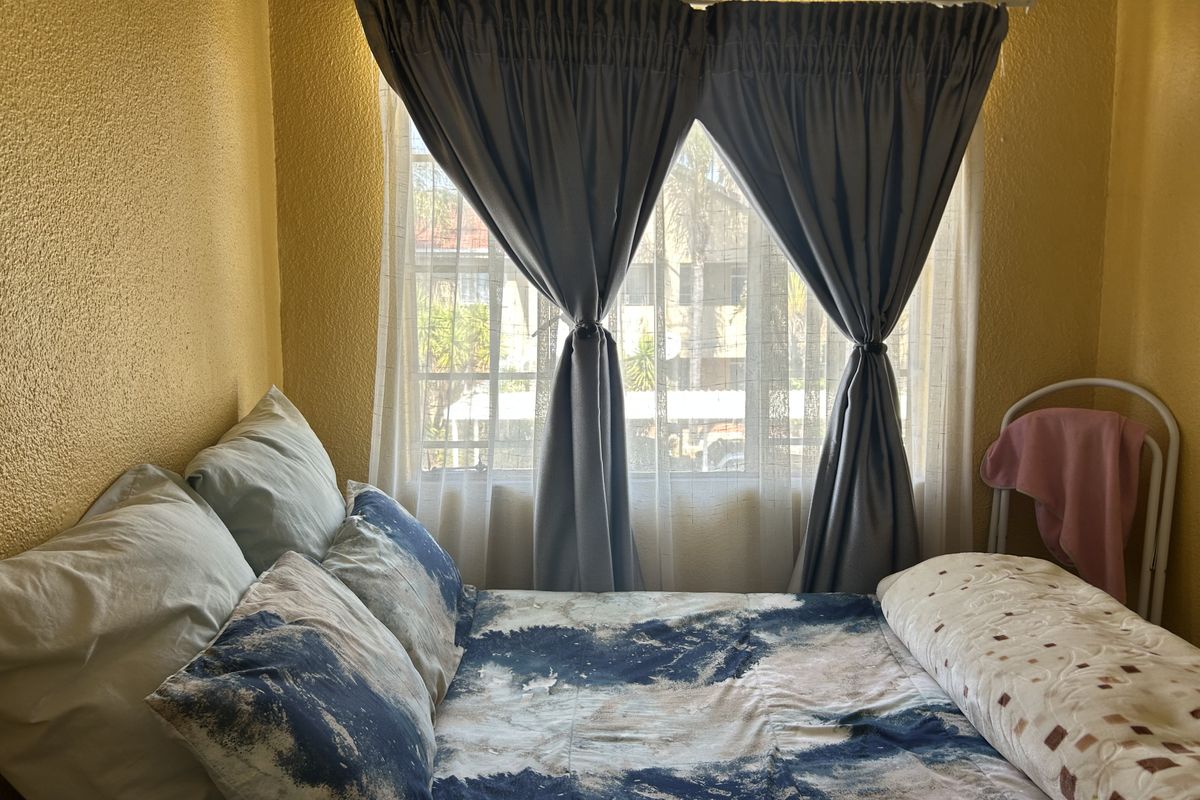 A bedroom featuring a window with a curtain rod, providing natural light and a view of the surrounding apartment complex.