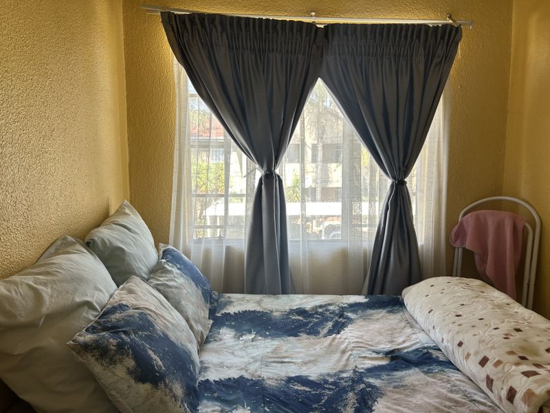A bedroom featuring a window with a curtain rod, providing natural light and a view of the surrounding apartment complex.