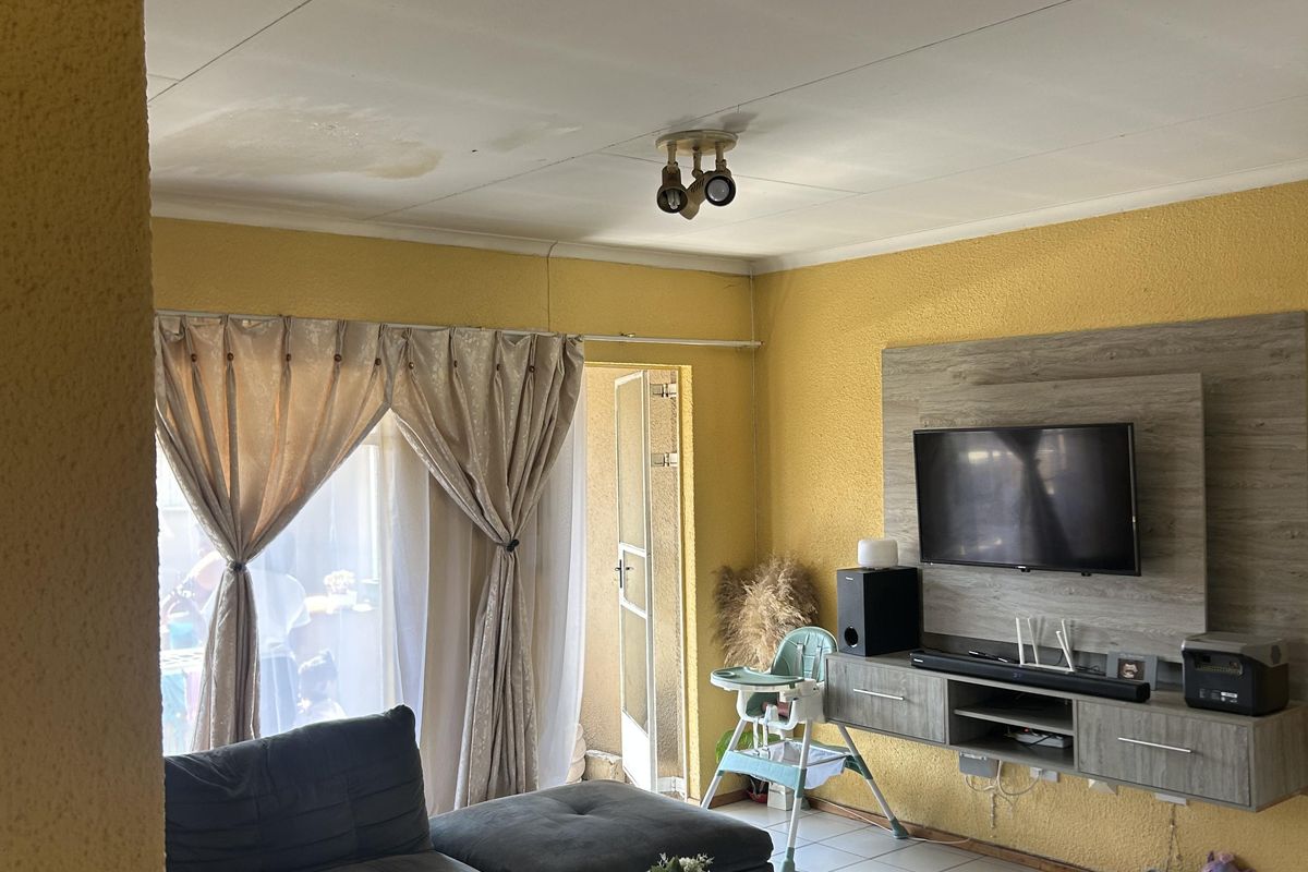 Living room featuring tiled flooring and a wall-mounted media unit, with visible ceiling water staining requiring attention.