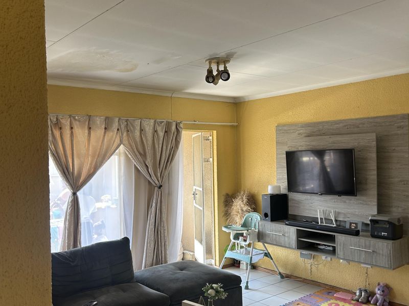 Living room featuring tiled flooring and a wall-mounted media unit, with visible ceiling water staining requiring attention.