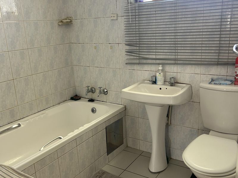 A functional bathroom featuring a bathtub, pedestal basin, and toilet with tiled finishes, currently requiring cosmetic updates to improve its overall condition.