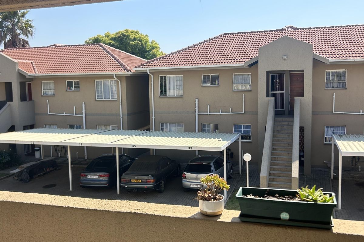 View from a balcony overlooking the apartment complex courtyard, featuring covered parking bays, tiled roof structures, and external staircases.